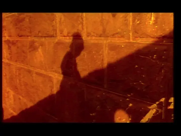 The shadow of a person in a hat falling across a stone block wall